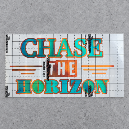 Chase the Horizon green and orange vinyl decal under gridded transfer tape on grey concrete