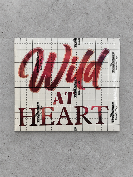 Wild at Heart vinyl decal in wine red with rose gold outline under transfer tape on grey concrete