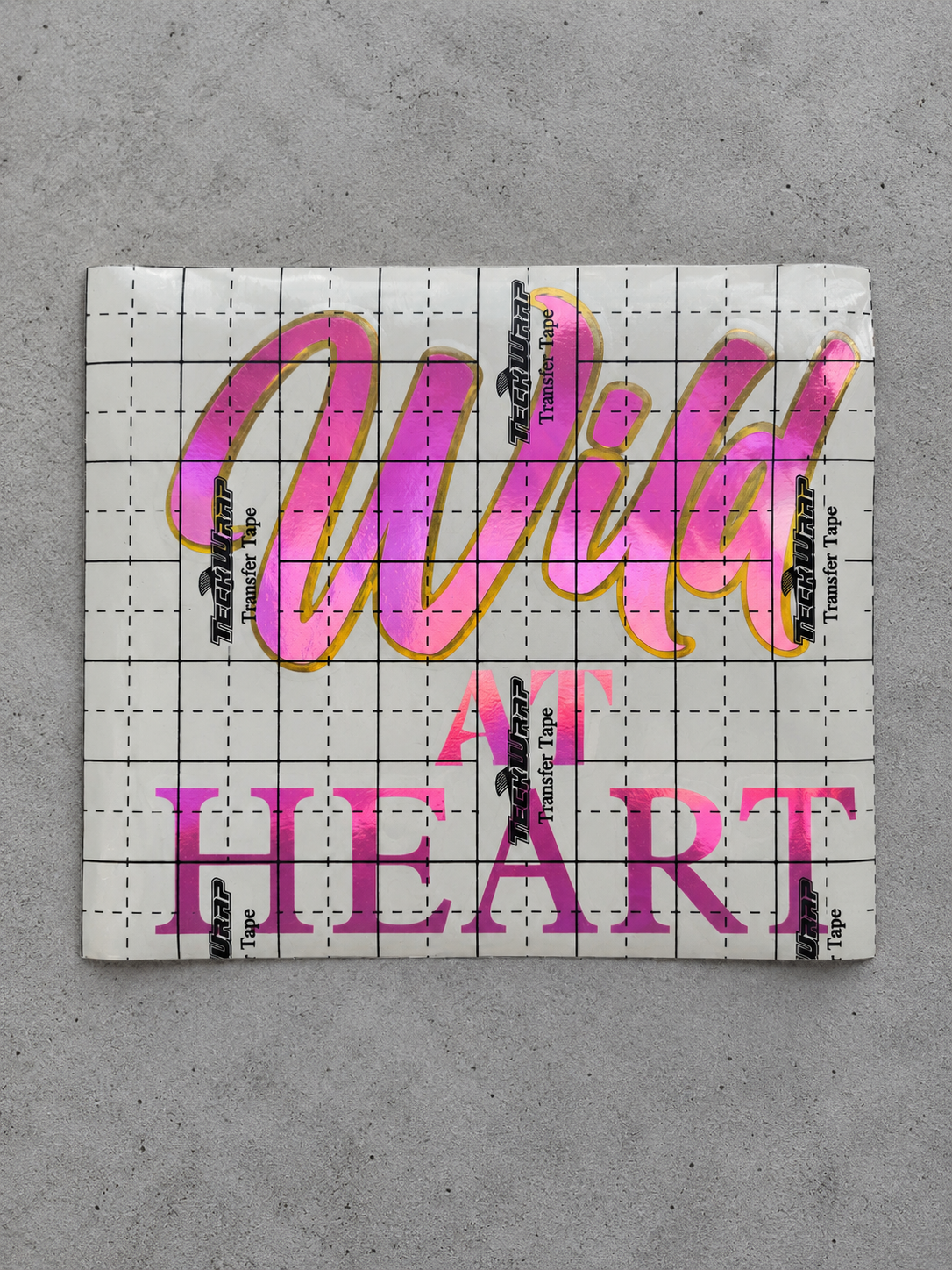 Wild at Heart vinyl decal in royal pink with prime gold outline under transfer tape on grey concrete