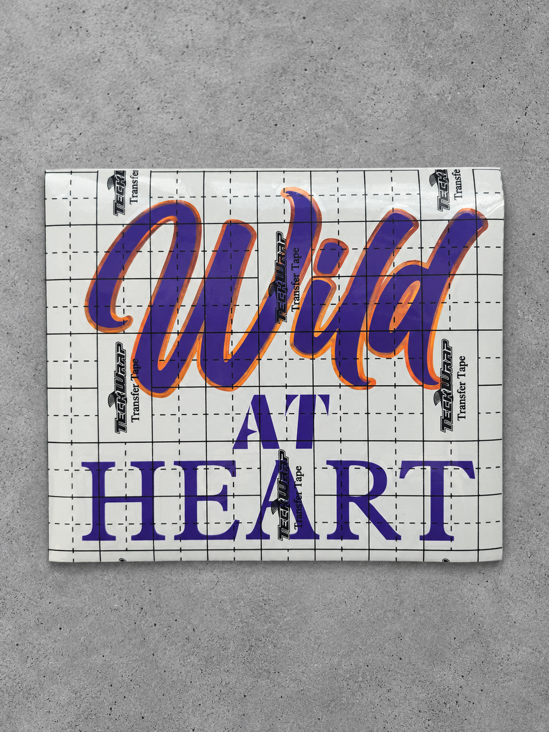 Wild at Heart vinyl decal in glossy purple with cayenne orange outline under transfer tape on grey concrete